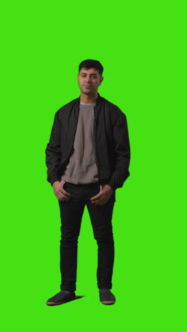 vertical video full length portrait shot of casually dressed young man standing against green screen folding arms