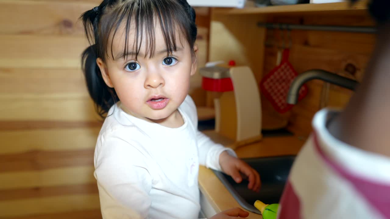 おもちゃのキッチンで遊び、おもちゃのトウモロコシを洗うかわいい幼い女の子