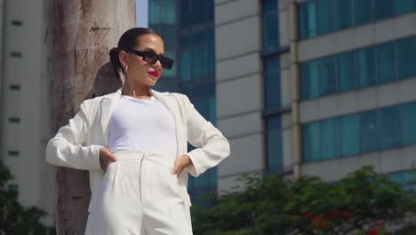 a young woman, donning a business suit, stands in the heart of the city with tall building in the background low angle