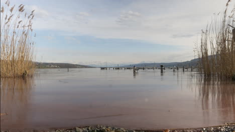 Zeitrafferaufnahme-Mit-Blick-Auf-Den-Lake-Hallwyl-Und-Schneebedeckten-Bergen-Im-Hintergrund