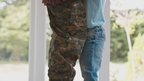 close up of loving army father in uniform home on leave with son standing on feet