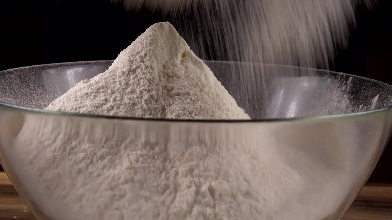 Peneirando farinha com uma peneira para uma tigela de vidro na cozinha