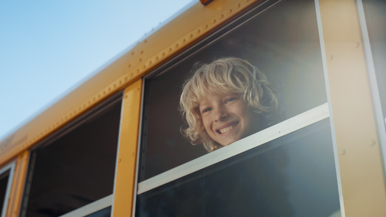 Glimlachende jongen kijkt uit het raam van de schoolbus, close-up. Leerling staat in het voertuig.