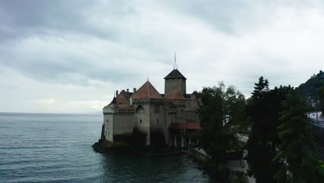 the drone camera is flying from behind chillon castle and the water waves are reaching the castle, the best beautiful castle in switzerland