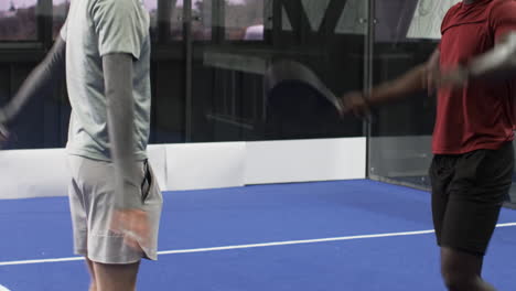 players on blue padel indoor court preparing for match, wearing athletic shoes