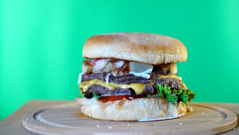 hamburguesa fresca y jugosa con queso, salsa y verduras girando en una tabla de madera frente al fondo de la pantalla verde.