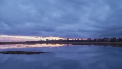 beautiful timelapse view of liepaja city skyline, lake liepaja in foreground, distant pedestrian apartment buildings, overcast evening with fast moving rain clouds, wide panoramic shot