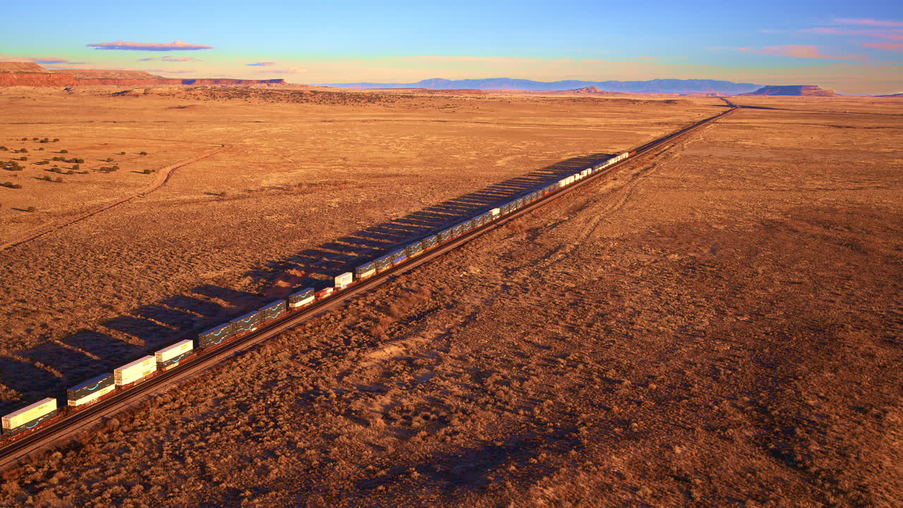 Cinematic drone shot freight train rolling through open western land, transportation logistics, rail infrastructure
