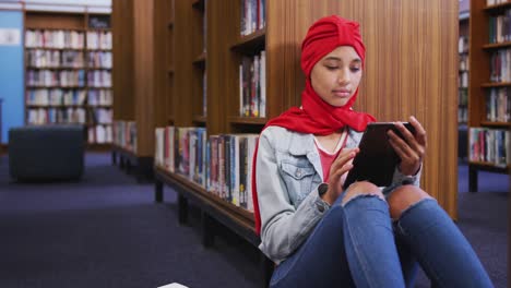 Eine-Asiatische-Studentin,-Die-Einen-Roten-Hijab-Trägt-Und-In-Einer-Bibliothek-Studiert-Und-Ein-Tablet-Benutzt