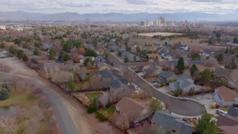 Aerial-over-homes-in-neighborhood-in-Reno,-Nevada-with-a-tilt-up-to-the-city-and-mountain-range-on-the-horizon