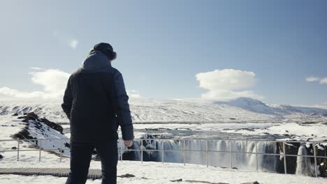 hombre caminando más cerca de la cascada de godafoss barrera de seguridad, día despejado en islandia