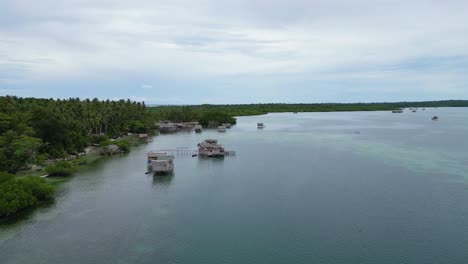 Aerial-dolly-passes-above-banca-and-tropical-huts-on-stilts-above-ocean-water