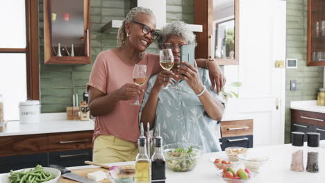 Felices-Amigas-Afroamericanas-Mayores-Bebiendo-Vino-Tomando-Selfies-En-La-Cocina,-Cámara-Lenta