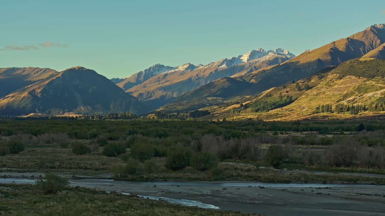 Foreste di pianura attraversate da fiumi poco profondi con la luce del sole che danza sulle montagne a Glenorchy
