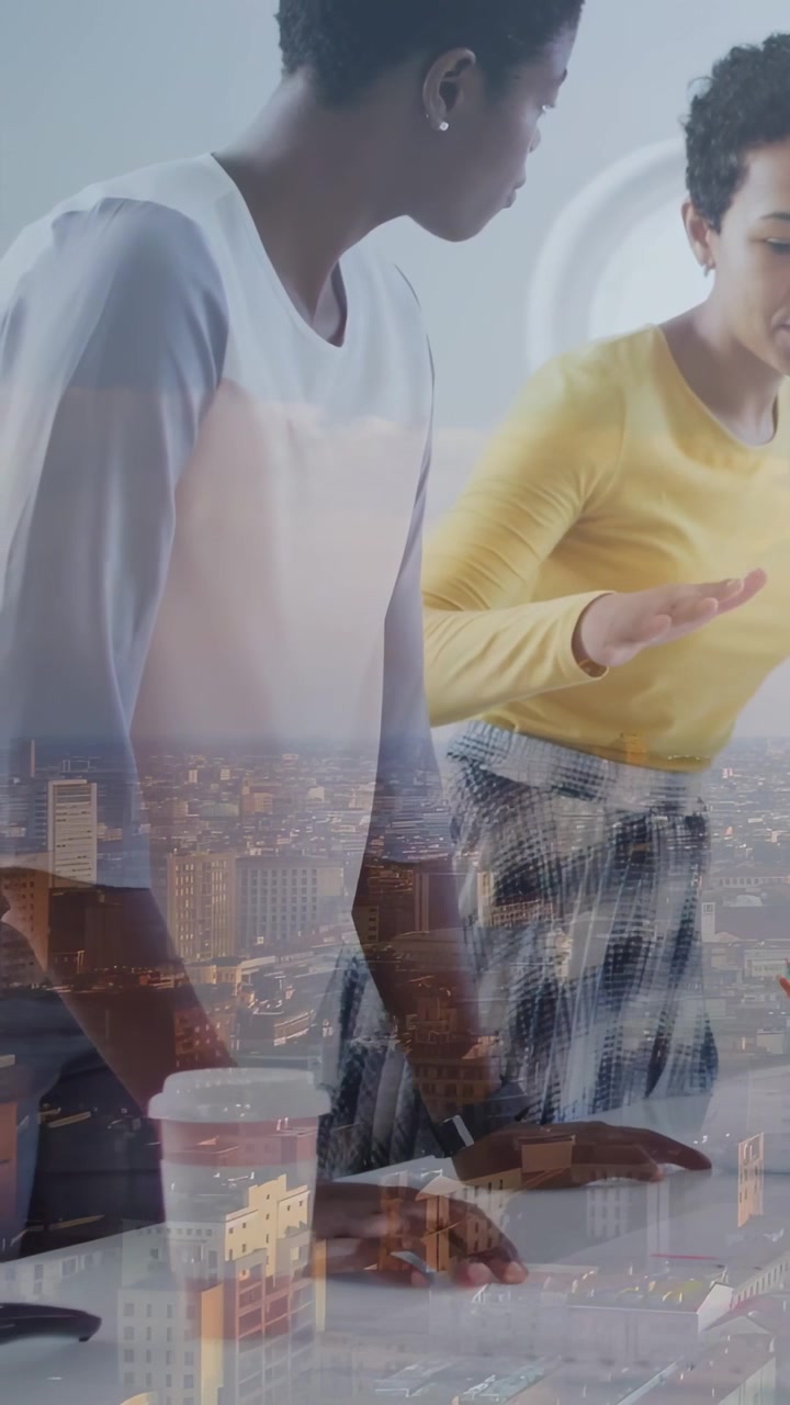 Video verticale: Donna a destra che indica, donna a sinistra che tocca modelli, pianificando la città, con una skyline sovrapposta.