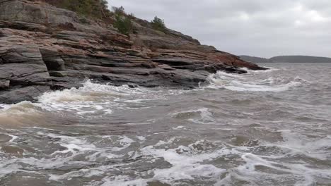 Grey-waves-lap-the-rocky-Swedish-shoreline-under-a-heavy-overcast-sky