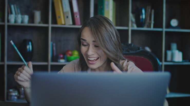 Lächelnde Geschäftsfrau blickt auf den Laptop-Bildschirm und freut sich über tolle Neuigkeiten