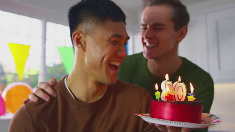 same sex male couple celebrating 30th birthday at home with cake and presents