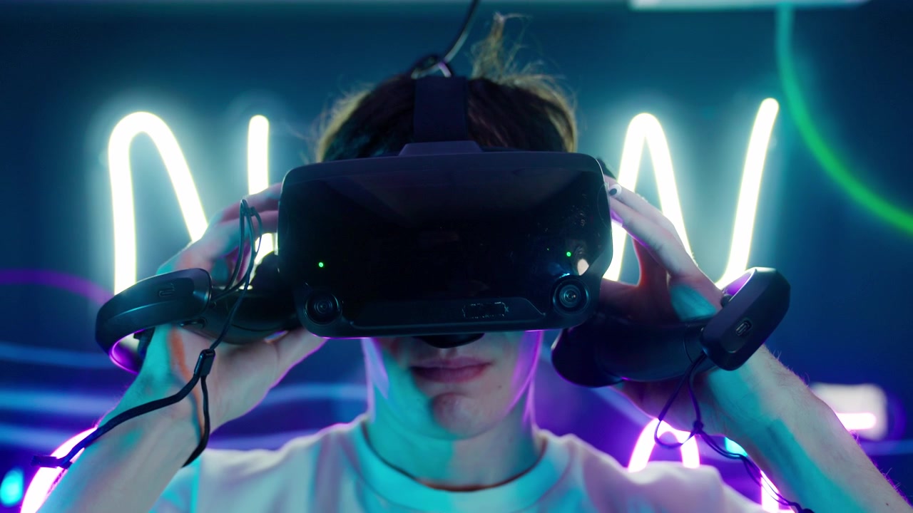 Giovane uomo con visore VR e controller in mano in una stanza al neon