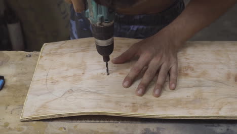 manos masculinas caucásicas perforando en una tabla de madera curva