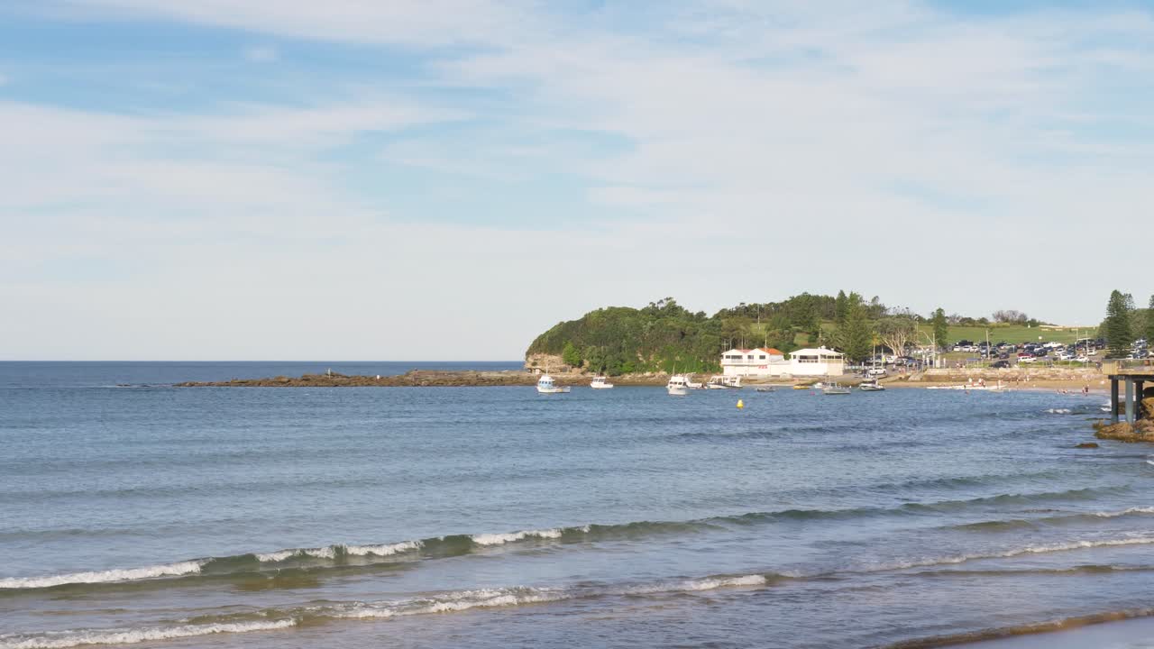 Slow motion landscape of The Haven Terrigal Beach with seaside waves breaking on sandy shoreline and fishing boats docked in waterfront harbour bay Central Coast Australia travel tourism marine