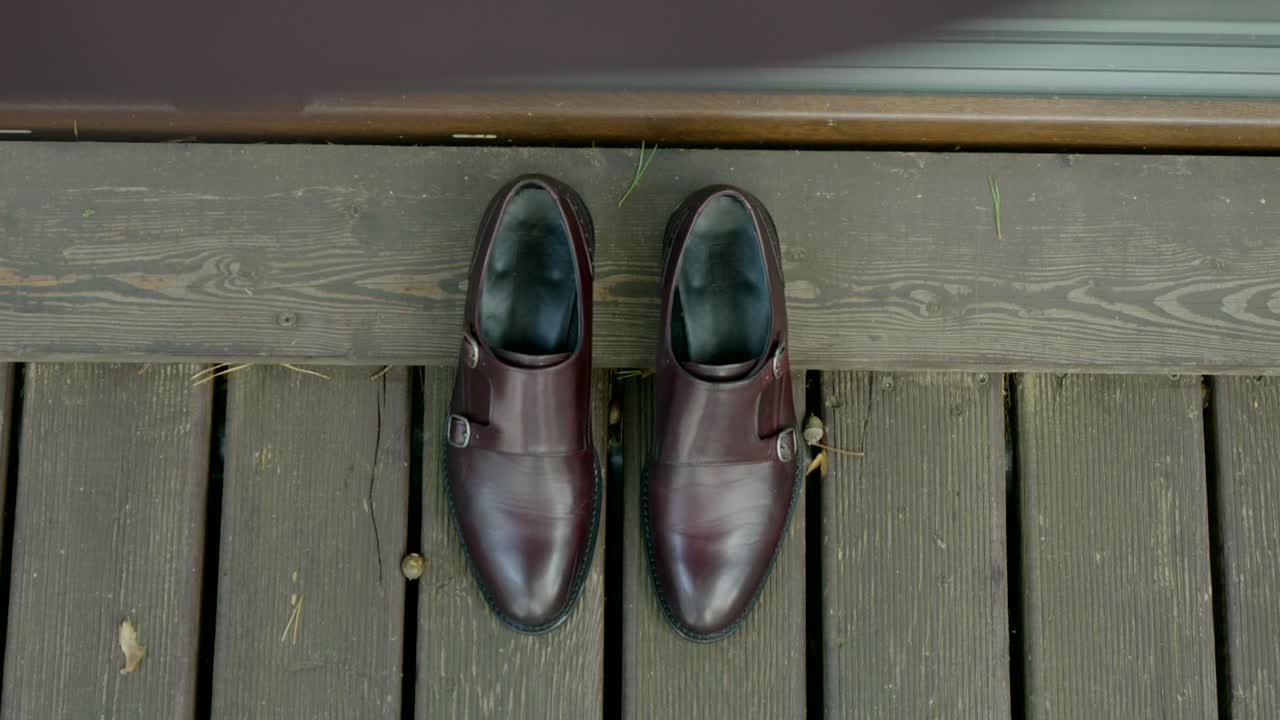 Close-up sepatu pengantin pria, berdiri di bawah jaket di atas platform kayu.