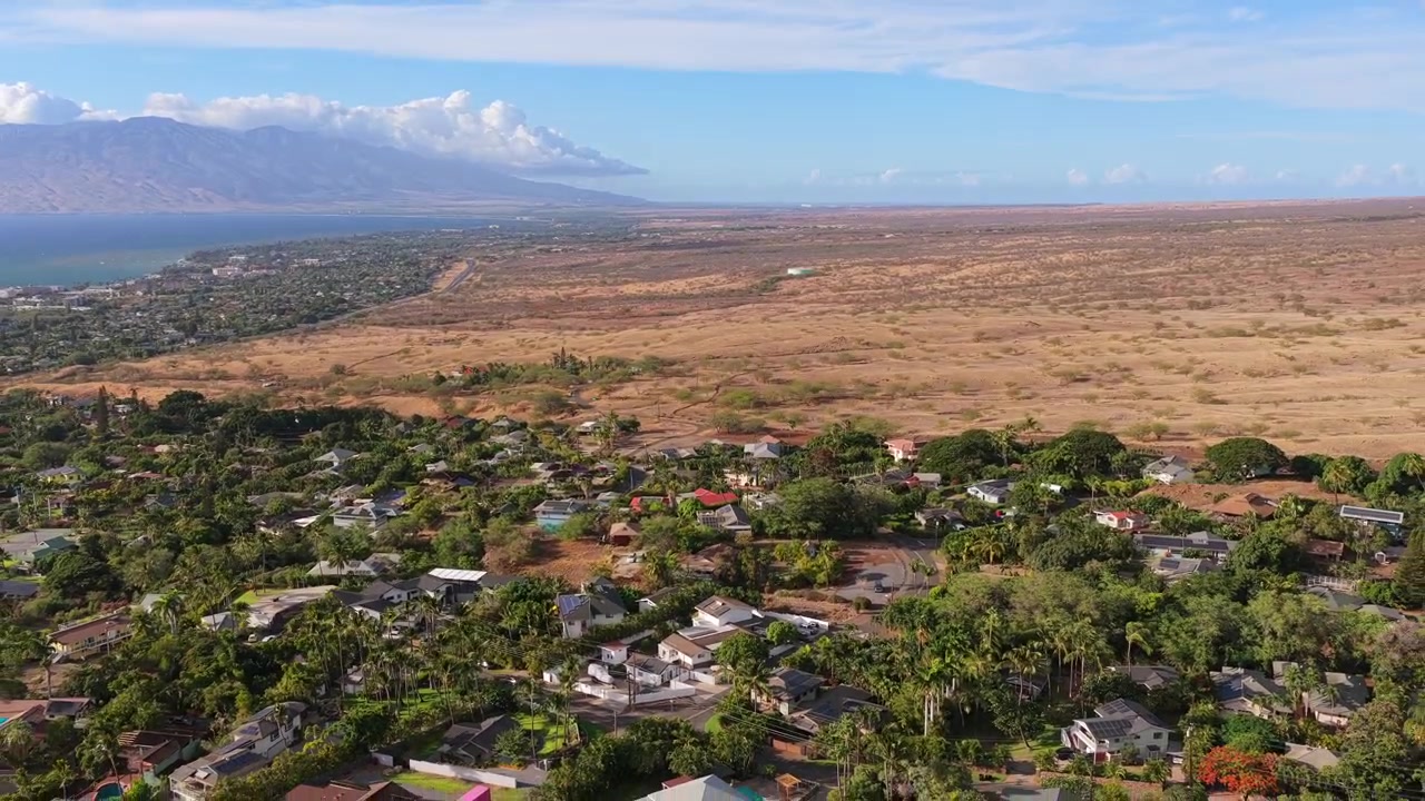 4K 60fps dronevideo af Maui Meadows ejendomme nær Wailea. Kameraet panorerer op og flyver tilbage fra en villavej for at afsløre luksushjem, frodige ejendomme og kystlinjen