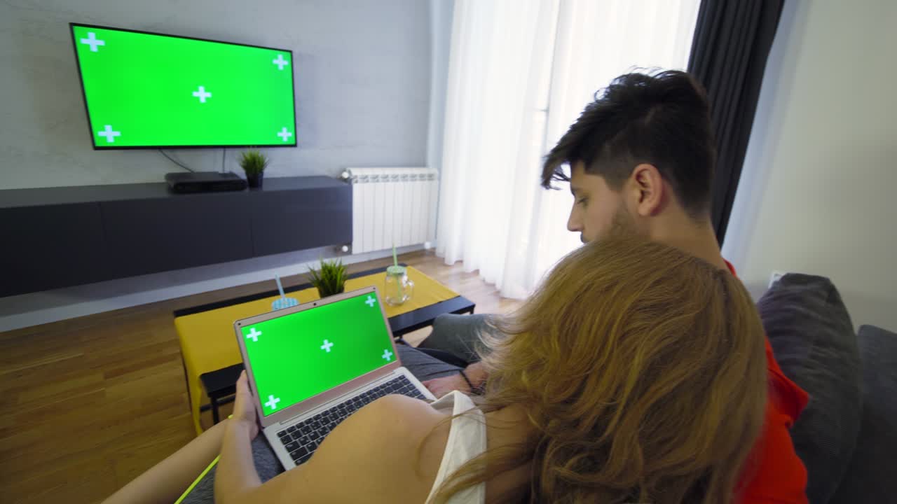 초록색 스크린 노트북과 tv가 있는 거실의 부부
