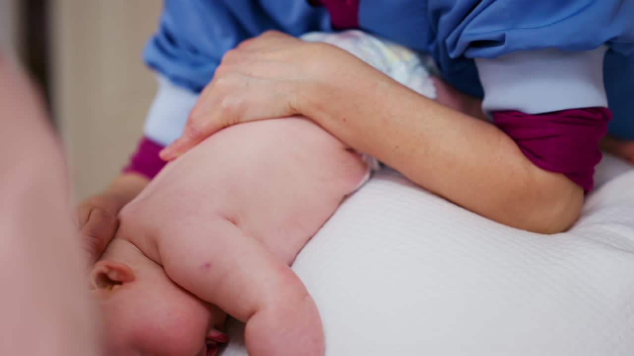 Baby placed on tummy on a stability ball while adults support the infant's torso and shoulders