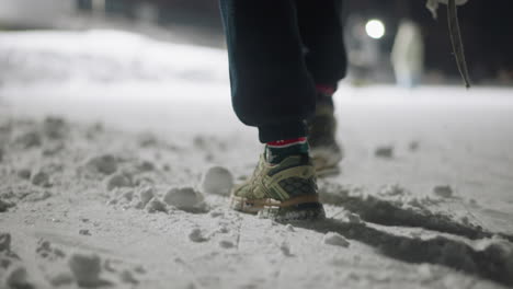 rear view of person walking on compact snow surface outdoors at night, wearing sneakers and socks, casting long shadow across icy ground with footprints marking path in cold winter setting
