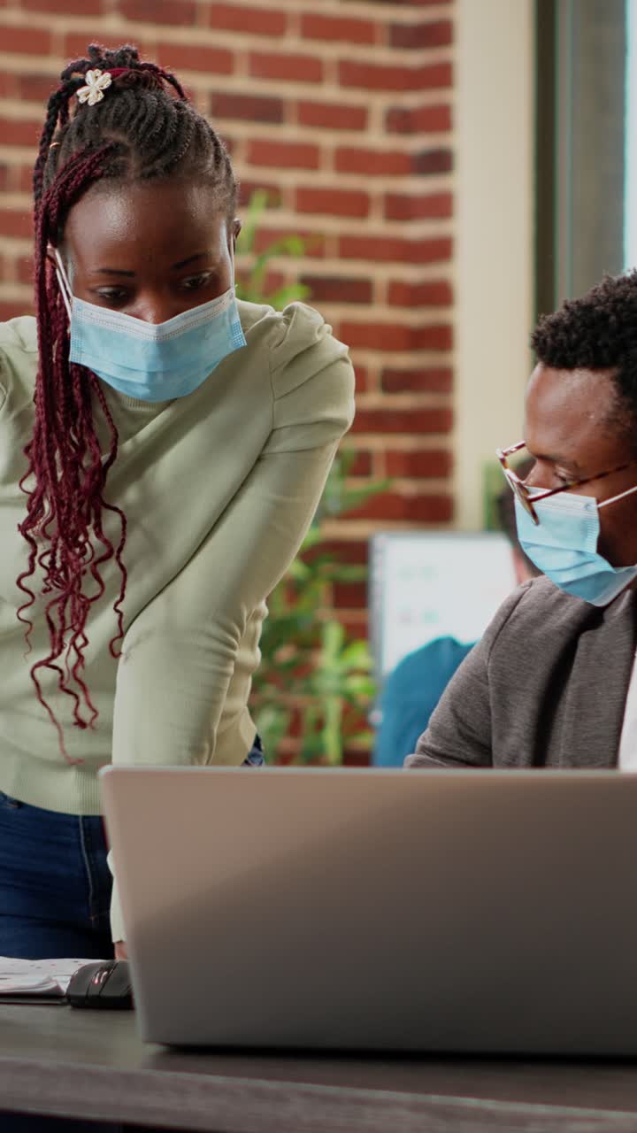 Office workers collaborating on a laptop wearing masks