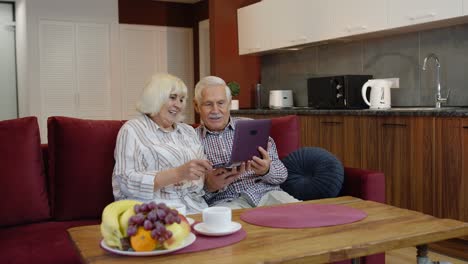 Pareja-De-Jubilados-Mayores-Con-Computadora-Portátil-Digital-En-Casa,-Descansando-En-Un-Sofá-En-Una-Acogedora-Sala-De-Estar