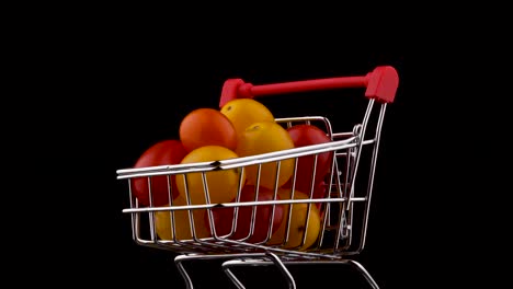 macro disparo de un carrito de supermercado lleno de tomates de uva rojos y amarillos. girando en la mesa giratoria. aislado en el fondo negro. primer plano.
