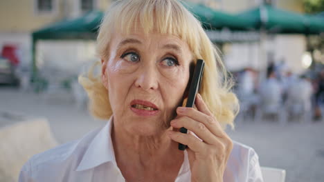 serious pensioner talking mobile phone on street close up. worried lady calling