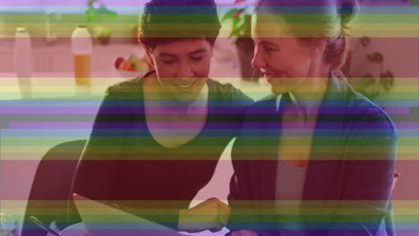 animation of pride rainbow stripes over happy caucasian lesbian couple using laptop at home