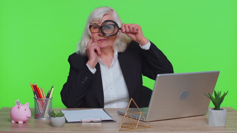 Investigator-senior-businesswoman-hold-magnifying-glass-near-face-looking-with-big-zoomed-funny-eye