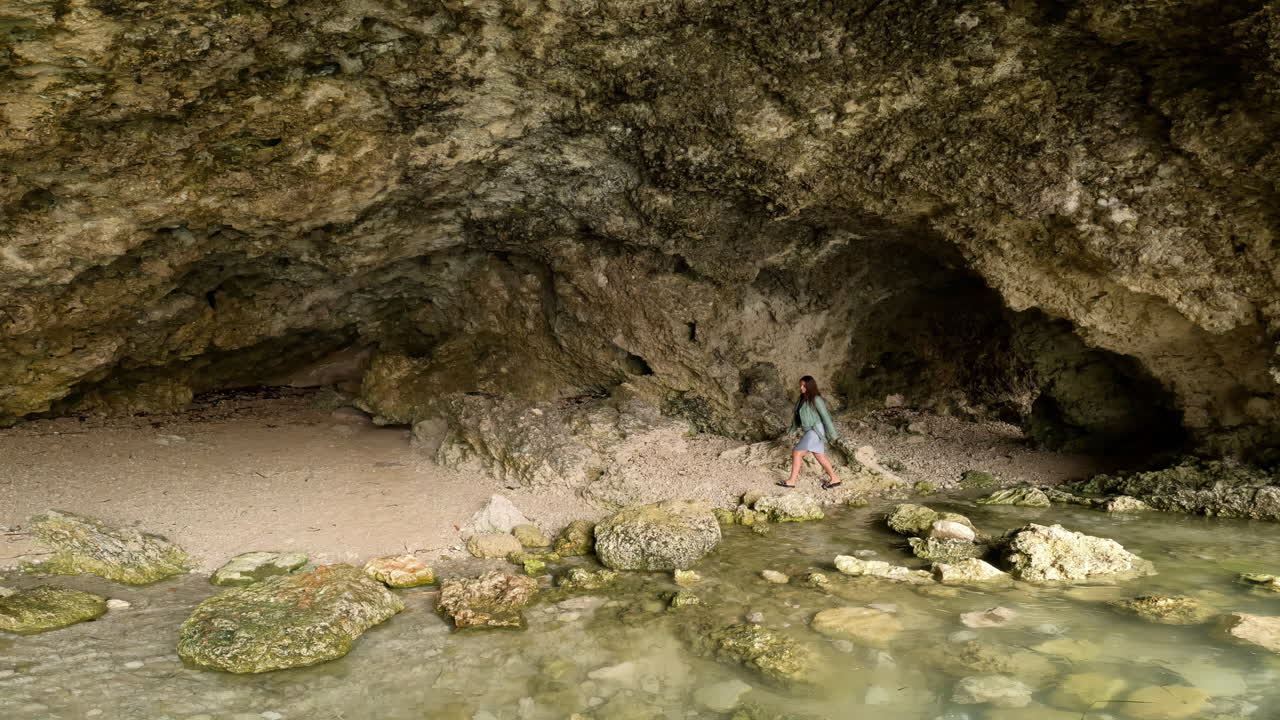 mujer camina a través de la costa de la cueva del mar explorando aguas claras y orillas rocosas