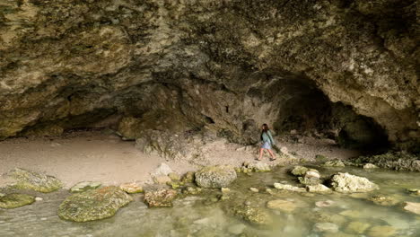 Woman-walks-through-sea-cave-coastline-exploring-clear-waters-and-rocky-shore