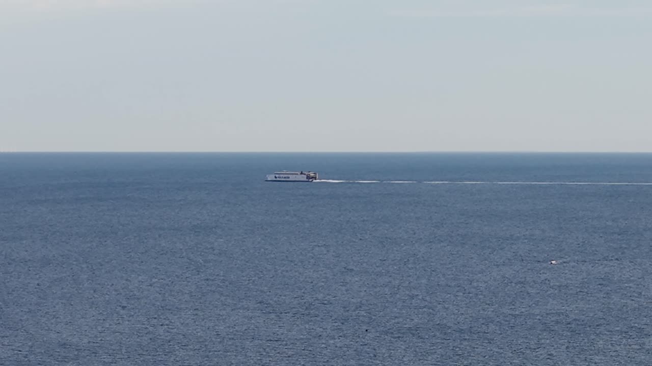 Aerial drone view of a cargo ship traveling across the open sea with calm blue water stretching to the horizon