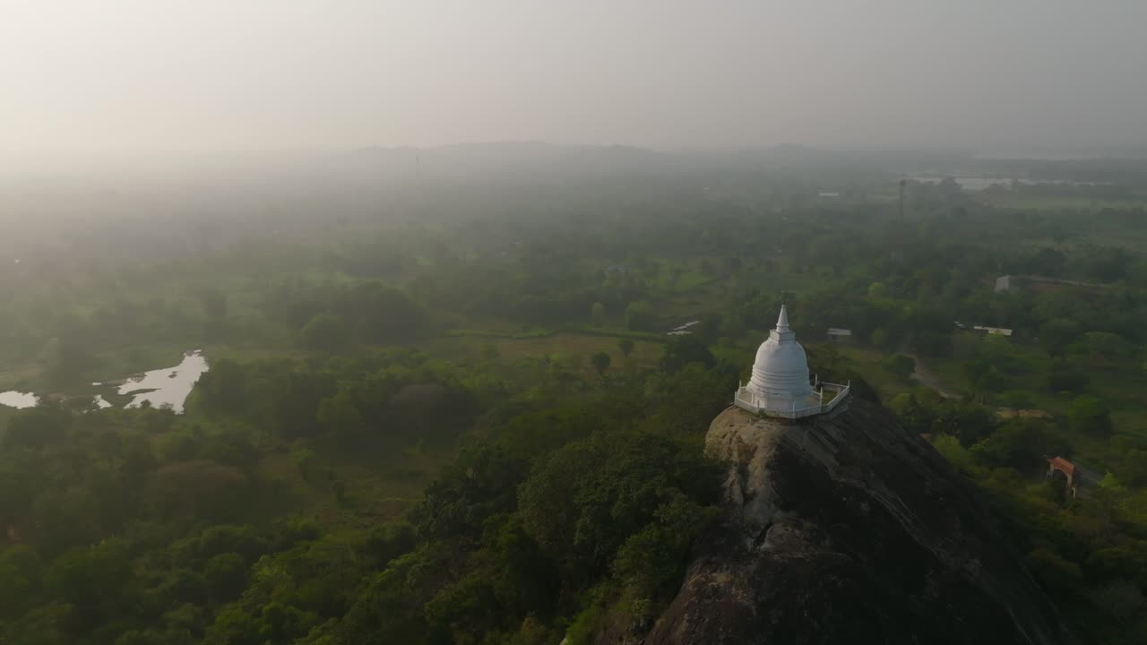 A serene white temple stands above the green canopy with misty plains beyond in Sri Lanka
