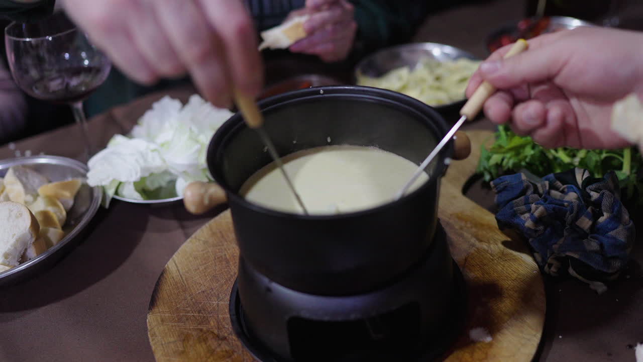 Hands dipping cauliflower into a creamy sauce as specialty of Bagna Cauda fondue at dinner table.