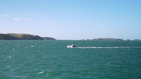 SLOWMO---Moving-shot-of-a-small-boat-on-turquoise-water-ocean-with-small-islands-in-background,-New-Zealand