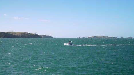 slowmo - moving shot of a small boat on turquoise water ocean with small islands in background, new zealand