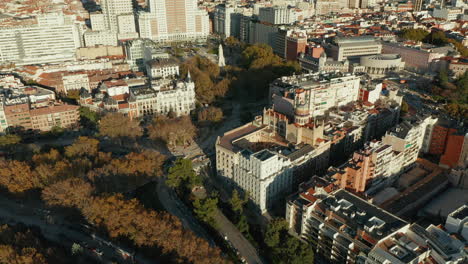 Descending-forwards-fly-above-park-in-town.-Aerial-view-of-historic-buildings-around-Plaza-de-Espana-with-high-Monument-to-Miguel-de-Cervantes.