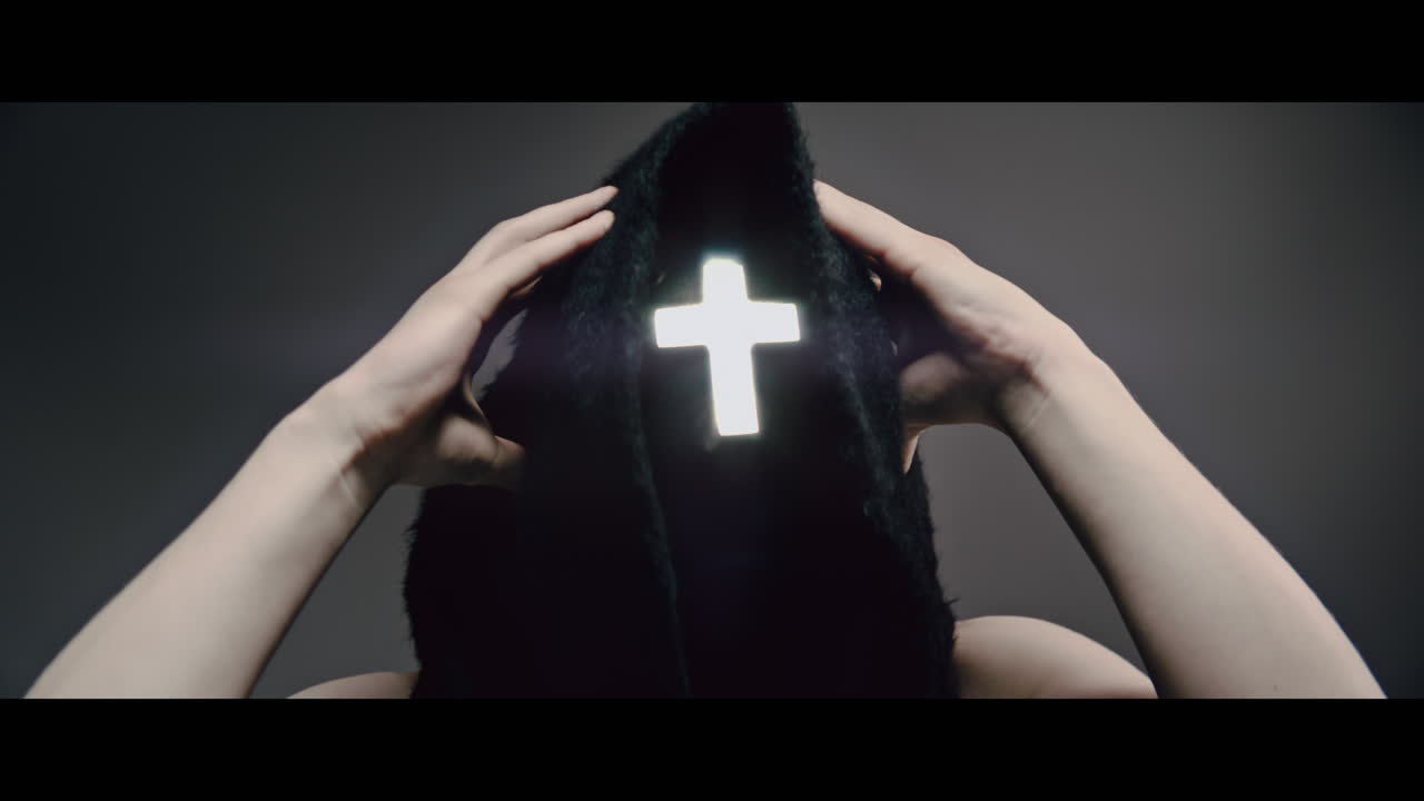 Masked man with cross of light glowing on his face grabs his head with his hand