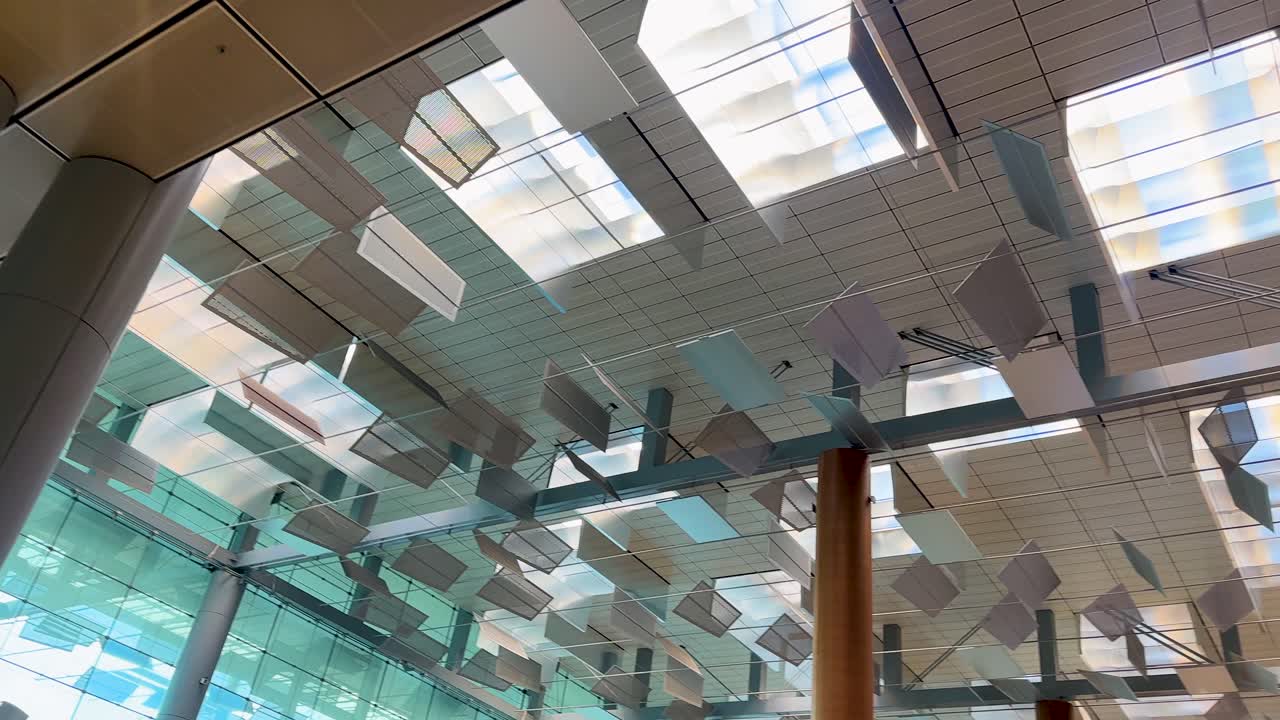 Upward camera movement reveals geometric ceiling panels, natural light, and reflective surfaces in airport interior