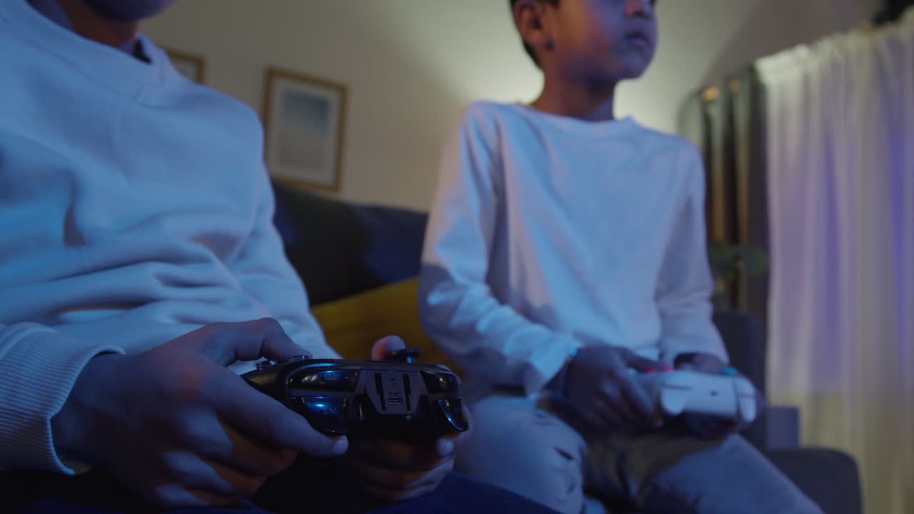 cerca de las manos de dos niños jóvenes en casa jugando con consola de juegos de computadora en la televisión sosteniendo controladores tarde en la noche 7