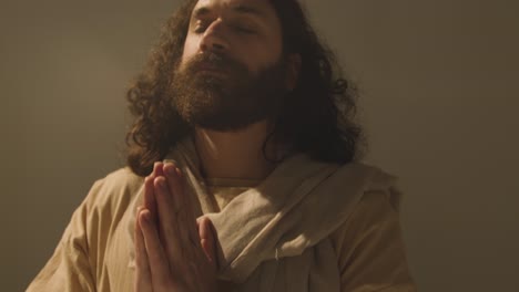 studio portrait of man wearing robes with long hair and beard representing figure of jesus christ praying 3