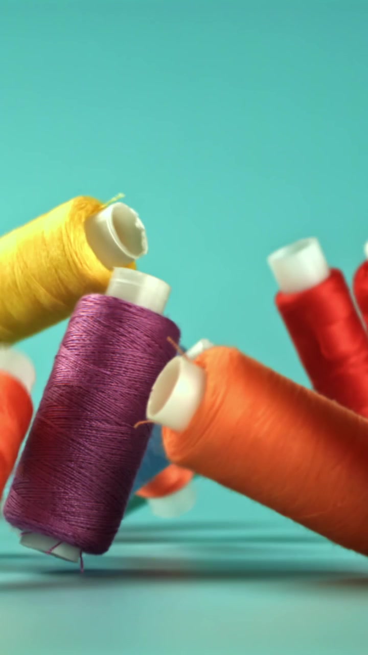 Colorful Thread Spools Falling and Landing on a Turquoise Surface