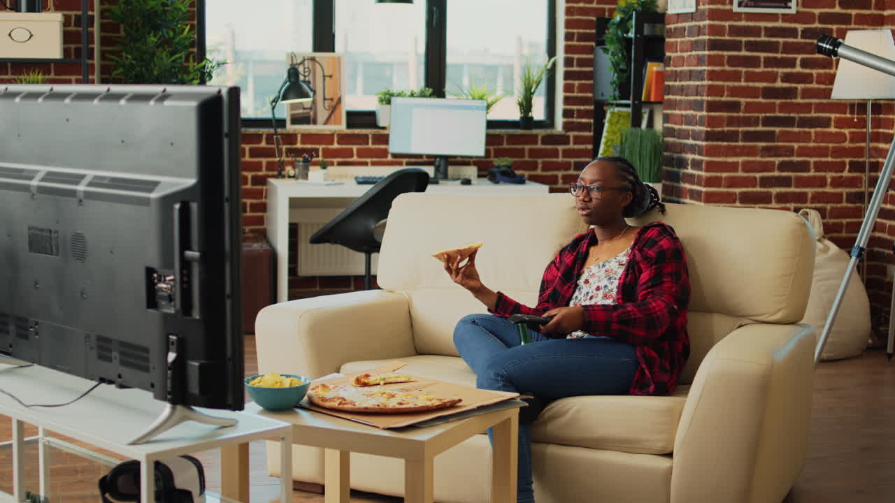 African american girl eating pizza slices and watching tv